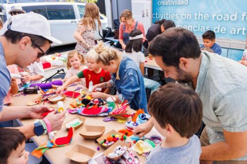 a group of adults and children gather around a table making sock puppets